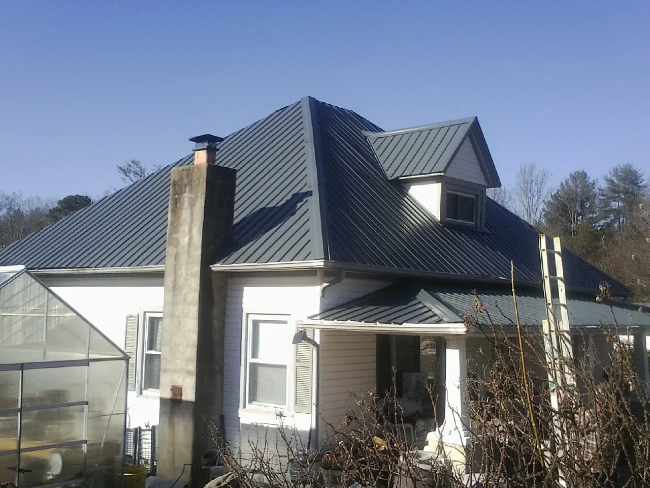 Dark blue standing seam metal roof on a white farmhouse with dormer — Slate & Tile Roof Repair by Roofing Brothers in Yorba Linda