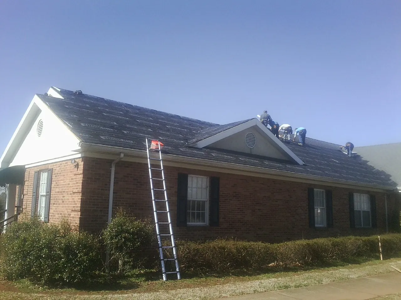 Crew tearing shingles off a brick ranch roof with a ladder set — Metal Roof Repair work by our crew in Yorba Linda