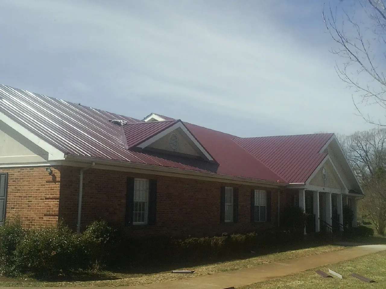 Red metal roof with gabled entries on a long brick building, from a Hail Damage Roof Repair job in Yorba Linda