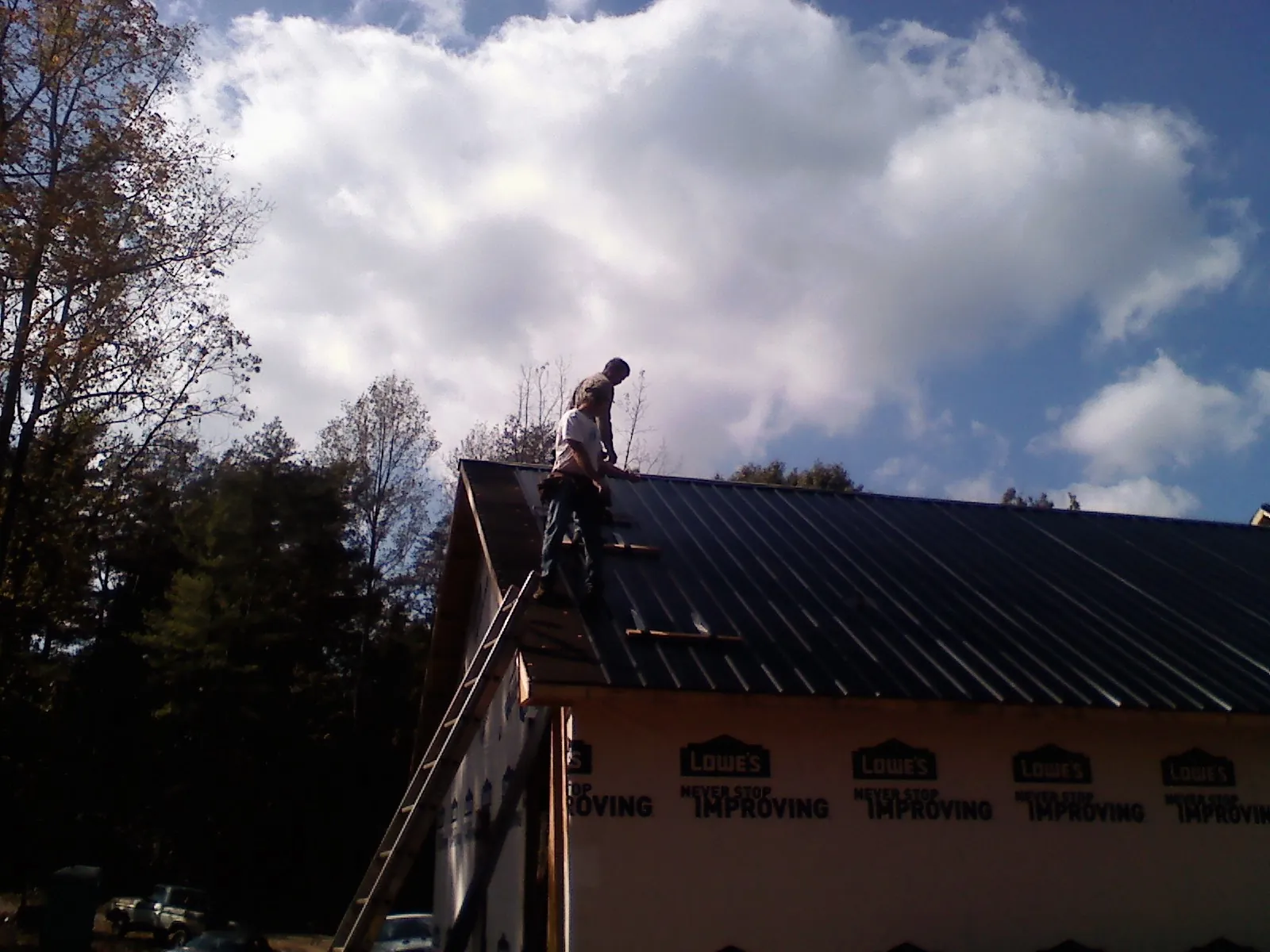 Roofer fastening dark metal panels high against a cloudy sky, from a Roof Inspection job in Yorba Linda