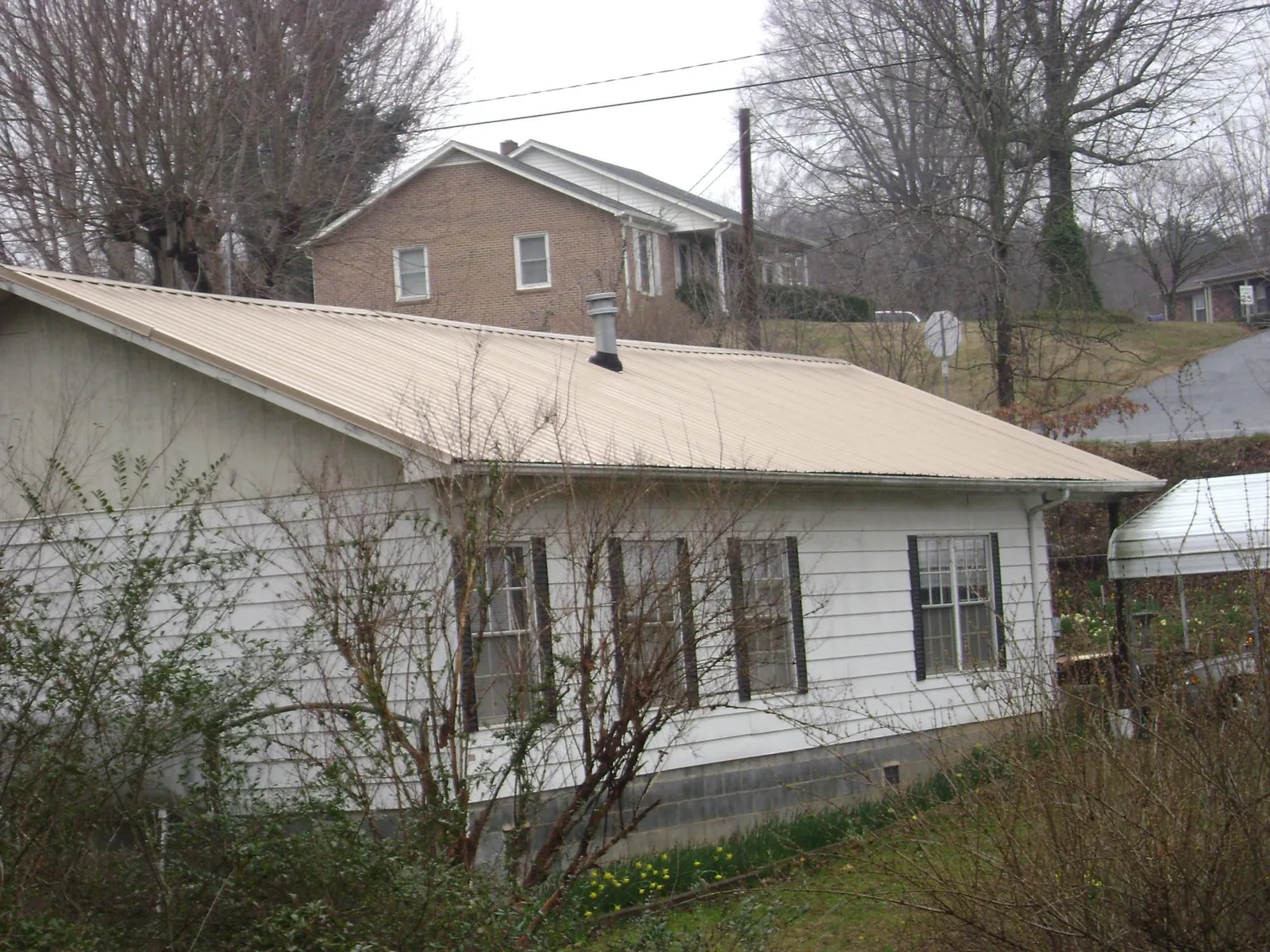 Tan metal roof on a white sided house set into a hillside — Commercial Roofing by Roofing Brothers in Yorba Linda